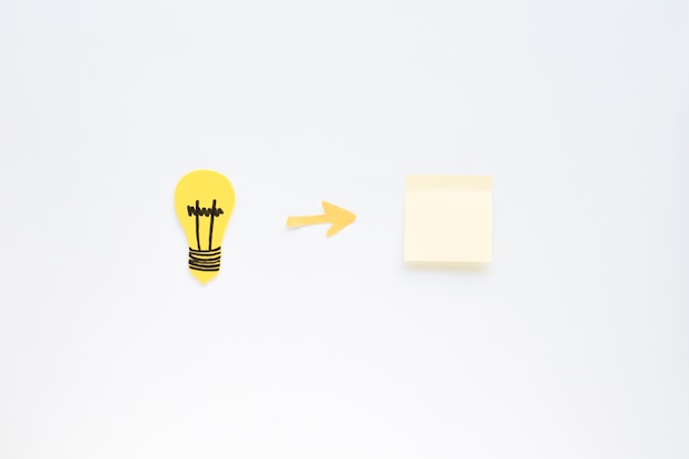 Free photo arrow symbol between light bulb and adhesive note on white background