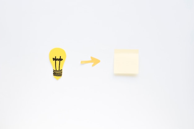Arrow symbol between light bulb and adhesive note on white background