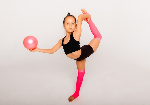 Художественная гимнастика. гибкая маленькая девочка выступает с мячом на белом фоне.