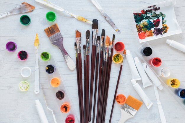 Art materials scattered on white table from above