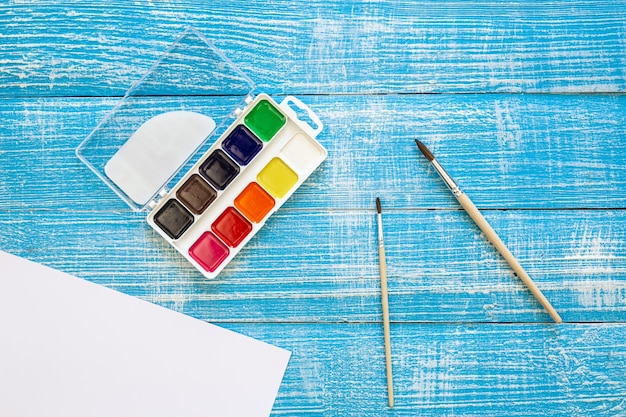 Art palette with paint and brushes on a blue wooden background workplace for creativity home teaching concept drawing