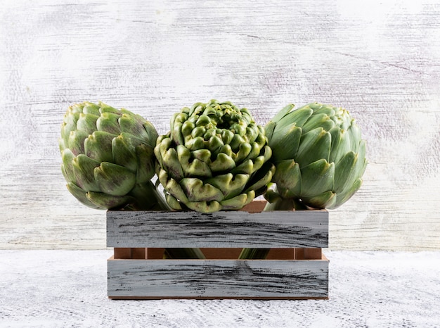 Artichoke in a wooden box on a light gray . side view.