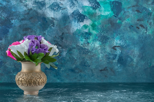 青い背景に、花瓶に人工のカラフルな花。