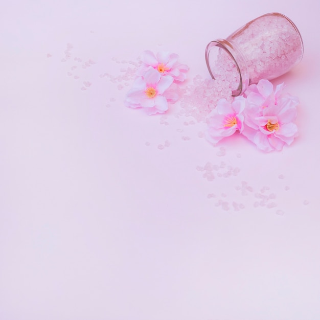 Artificial flowers and spilled salt from jar on pink background