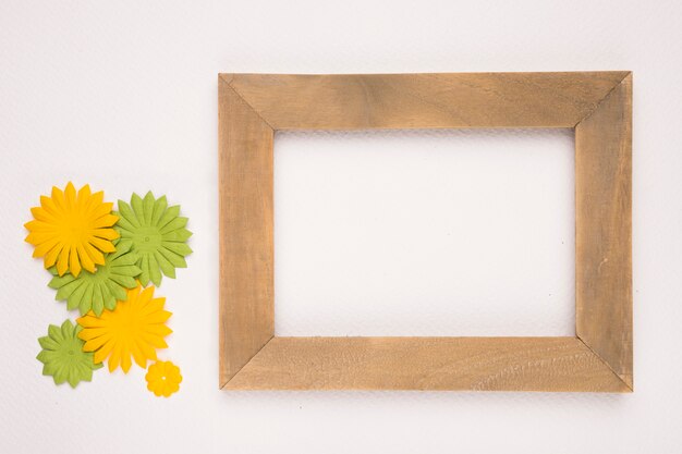Artificial green and yellow flowers near the wooden empty frame on white backdrop