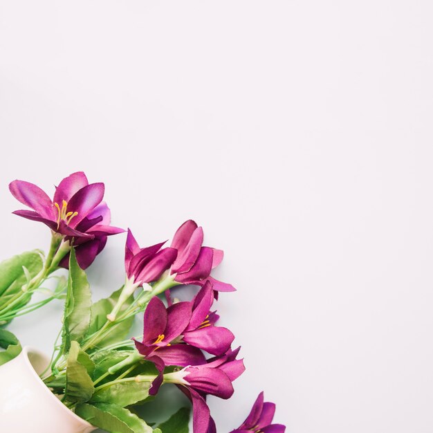 Artificial purple flowers in vase on white backdrop