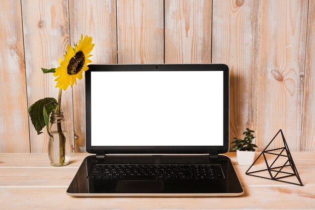 Artificial sunflower in vase with laptop on wooden table