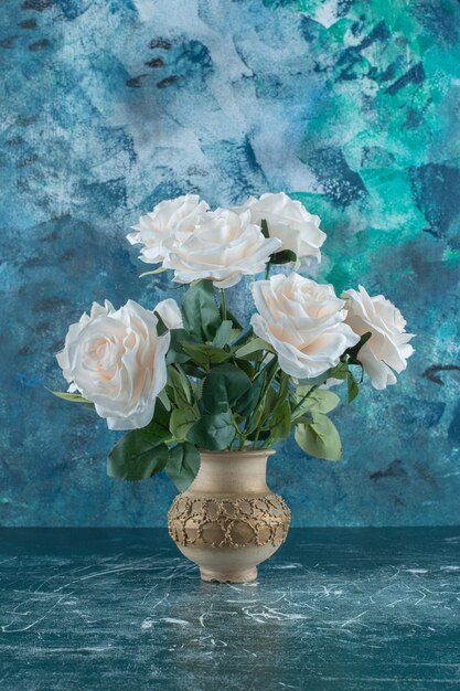 Artificial white roses in a vase , on the blue background.