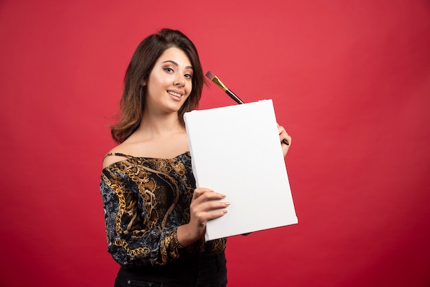 Free photo artist girl holding her artwork on canvas and demonstrating it to the public.