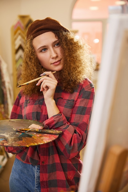 Artist holds a brush and is looking at her work