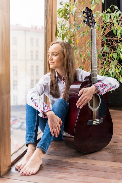 Foto gratuita artista in casa tenendo la chitarra e guardando attraverso le finestre