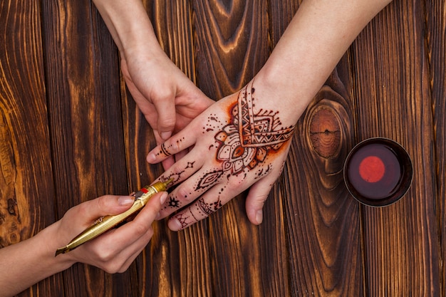 Artist making mehndi on womans hand near tea cup