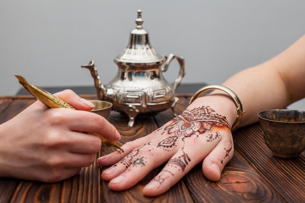 Artist making mehndi on womans hand near teapot