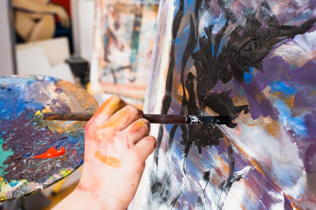 Artist's hand painting with black brushstroke on canvas