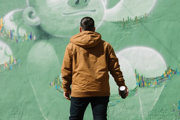 Художник, стоящий перед стенами граффити с аэрозолем, может в руке