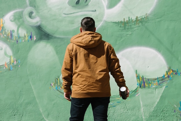 エアロゾルの入った落書き壁の前に立っているアーティストが手に取ることができます