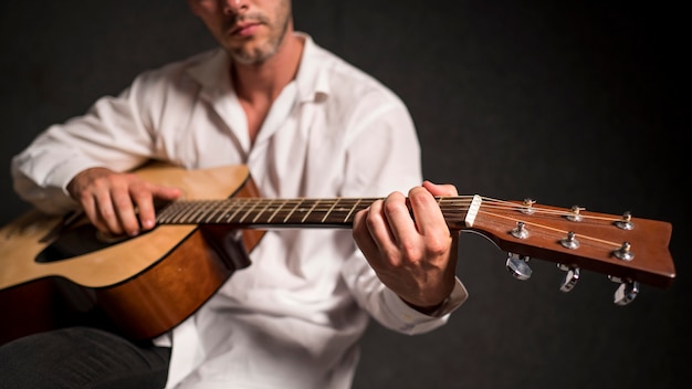 Художник в белой рубашке играет на акустической гитаре в студии