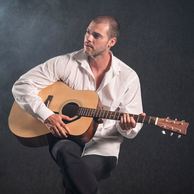 Художник в белой рубашке играет на гитаре и смотрит в сторону
