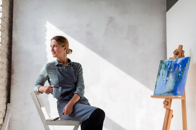 Artist woman posing on chair with canvas