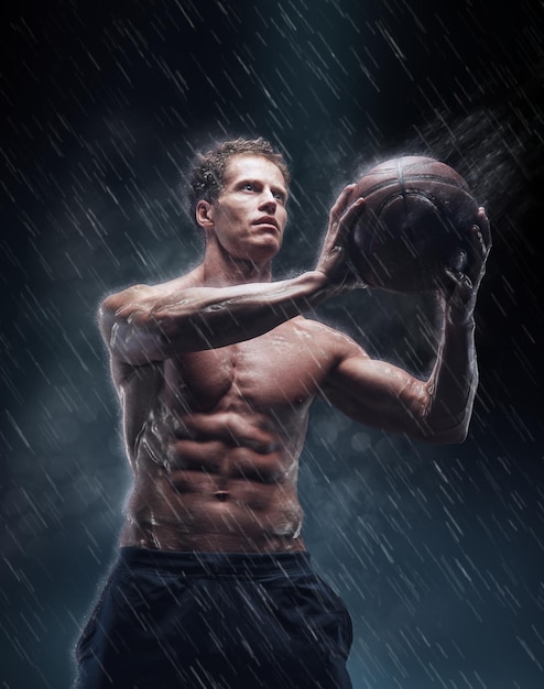 Artistic portrait of shirtless wet bascetball player under droplets.