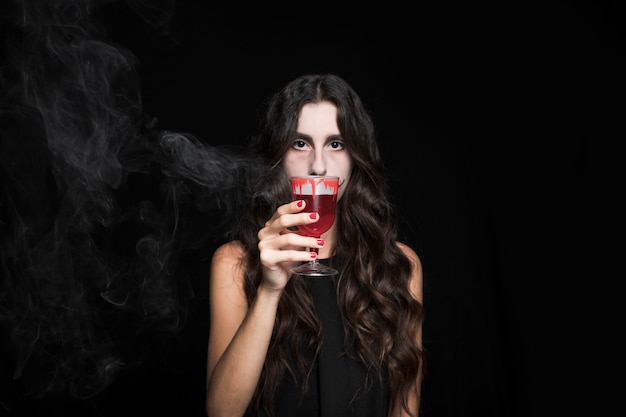 Free photo ashy woman closing face by goblet with smoking red liquid