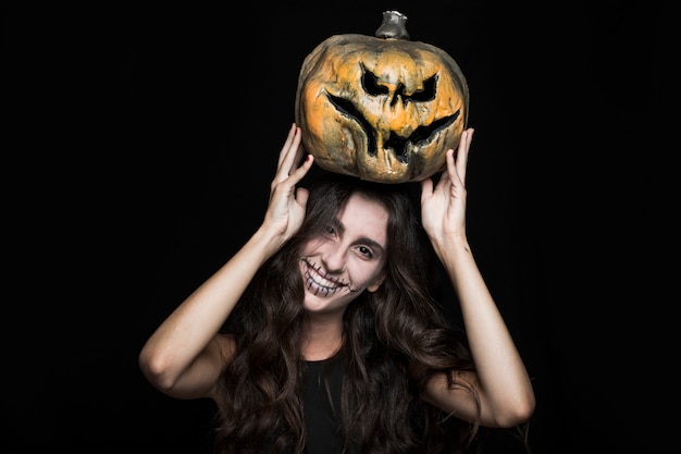 Free photo ashy woman with halloween pumpkin above head