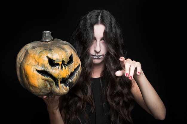 Free photo ashy woman with upping hand holding halloween pumpkin