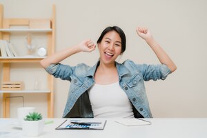 Asia business woman success celebration keeping arms raised at home office.