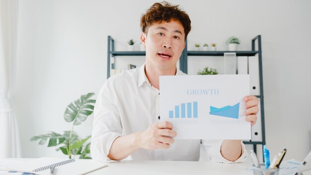 Free Photo asia businessman social distancing in new normal situation for virus prevention looking at camera presentation to colleague about plan in video call while work in office.