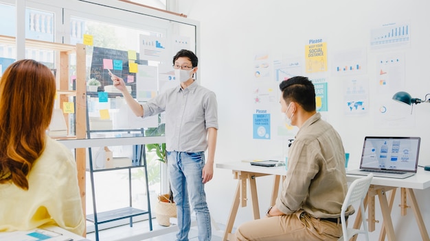 Gli imprenditori asiatici che incontrano idee per il brainstorming conducono idee per presentazioni aziendali proiettano colleghi e indossano una maschera protettiva nel nuovo ufficio normale. stile di vita e lavoro dopo il coronavirus.