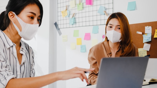 새로운 프로젝트 동료에 대한 아이디어를 브레인 스토밍하고 새로운 일반 사무실에서 보호용 안면 마스크를 착용하는 컴퓨터 프레젠테이션 회의를 사용하는 아시아 기업인.