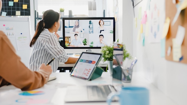 Asia businesspeople using desktop talk to colleagues discussing business brainstorm about plan in video call meeting in new normal office.