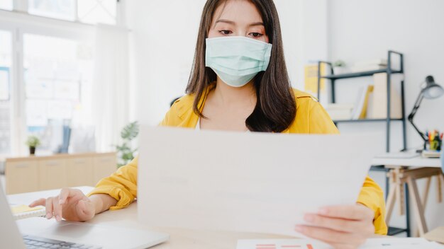 사무실에서 직장에서 노트북을 사용하는 동안 바이러스 예방을위한 새로운 정상적인 상황에서 사회적 거리를두기 위해 의료 얼굴 마스크를 착용하는 아시아 사업가 기업가. 코로나 바이러스 이후의 생활 방식.
