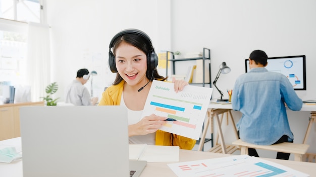 Asia imprenditrice sociale allontanamento in una nuova situazione normale per la prevenzione dei virus durante l'utilizzo di laptop presentazione ai colleghi sul piano in videochiamata mentre si lavora in ufficio. la vita dopo il virus corona.