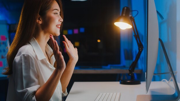 Asia businesswoman using computer talk to colleagues about plan in video call while working from home at living room at night. Self-isolation, social distancing, quarantine for coronavirus prevention.