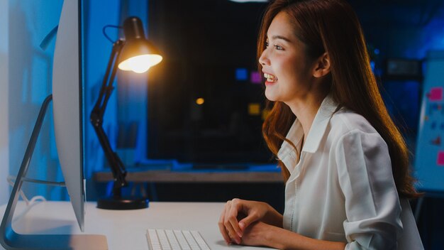 Asia businesswoman using computer talk to colleagues about plan in video call while working from home at living room at night. Self-isolation, social distancing, quarantine for coronavirus prevention.