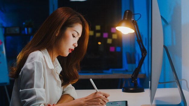 Asia businesswoman using computer talk to colleagues about plan in video call while working from home at living room at night. Self-isolation, social distancing, quarantine for coronavirus prevention.