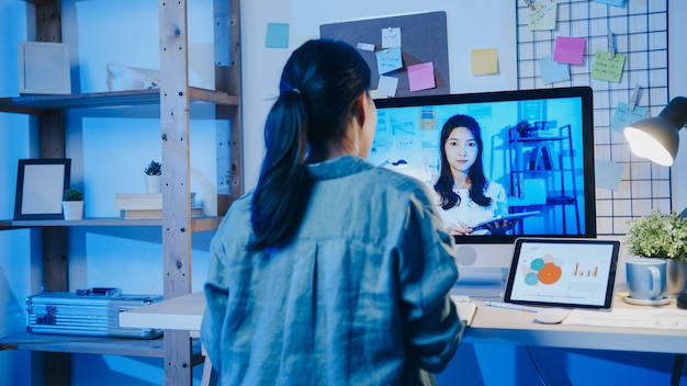 Foto gratuita la donna d'affari asiatica che utilizza il desktop parla con i colleghi del piano nella riunione di videochiamata in soggiorno