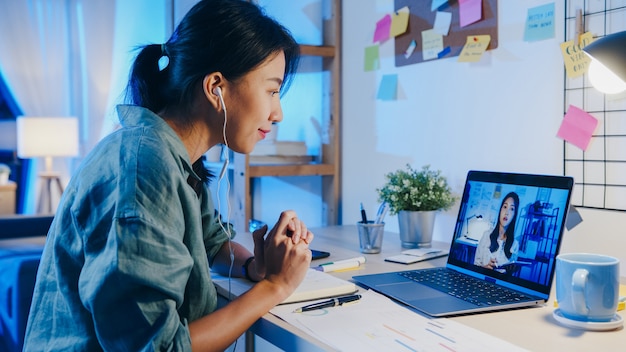 Asia businesswoman using laptop talk to colleagues about plan in video call meeting at living room.