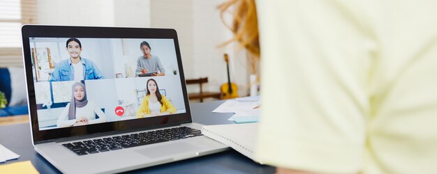 Asia businesswoman using laptop talk to colleagues about plan in video call meeting while working from home at living room. Self-isolation, social distancing, quarantine for corona virus prevention.