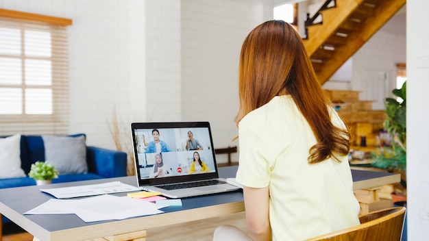 Asia businesswoman using laptop talk to colleagues about plan in video call meeting while working from home at living room. self-isolation, social distancing, quarantine for corona virus prevention.