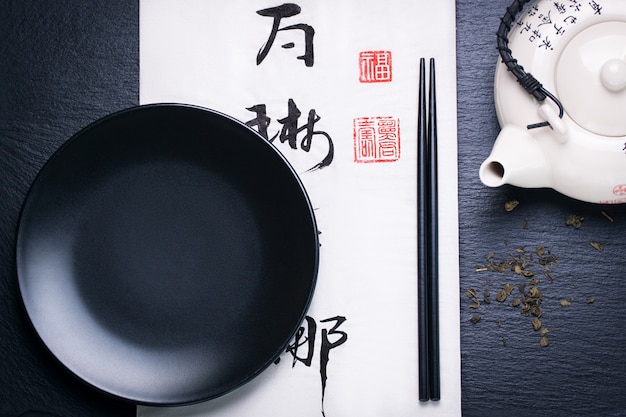 Asia food composition with chinese chopsticks and empty plate on a dark stone background