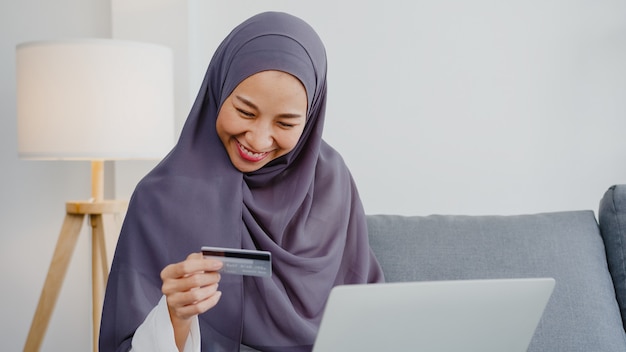Asia muslim lady using laptop, credit card buy and purchase e-commerce internet in living room at house.