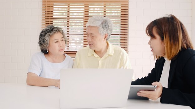 Asia smart female agent offers health insurance for elderly couples by document, tablet and laptop. 