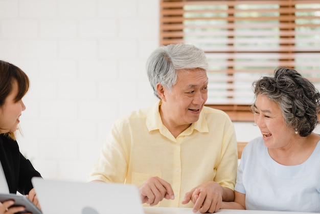 Asia smart female agent offers health insurance for elderly couples by document, tablet and laptop.