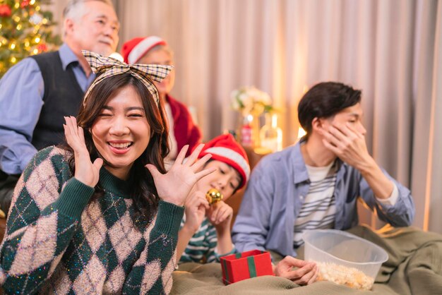 アジアの成人男性がクリスマス休暇中に親にプレゼントボックスを贈りながら、スマートフォンを使ってソファソファのリビングルームで一緒に自分撮り写真の幸せを話します家族関係の家のインテリアを結合します