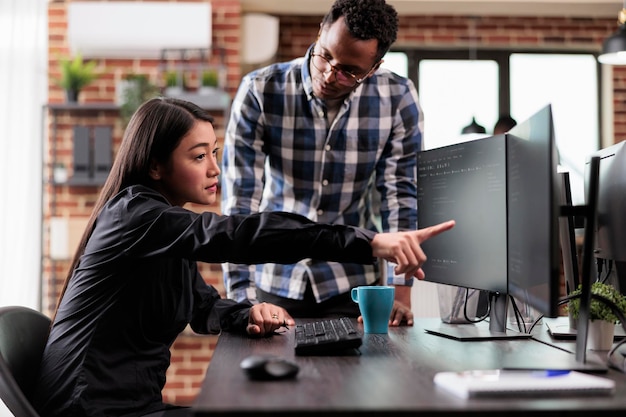 Asian application developer pointing out cloud database processing algorithm error while uploading network information. Multiethnic tech software engineers decrypting retrieved stolen data.