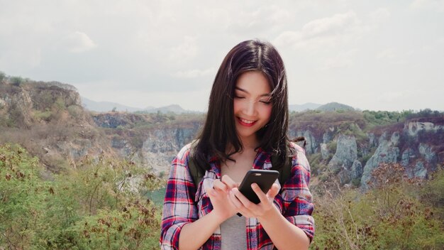 Asian backpacker woman on top of mountain, young female happy using mobile phone enjoy holidays on hiking adventure. 