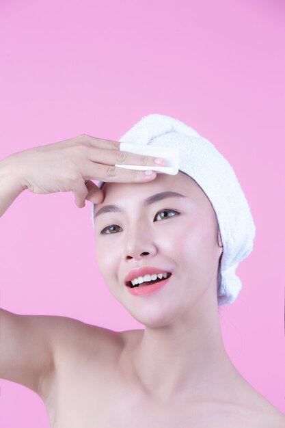 Asian beautiful woman wiping the face on a pink background, Cosmetology and Spa .