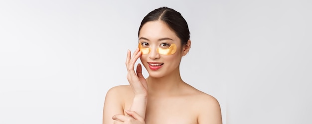 Азиатская красавица-подросток заботится о своей коже с золотыми глазными масками с заплатками под глазами